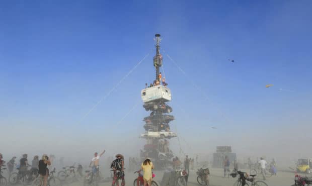 FILE -  this Monday, Aug. 27, 2018 file photo, burners surrounded by playa dust climb onto an art i...