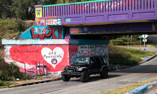 A vehicle drives by a tribute to victims of the Naval Air Station Pensacola that was freshly painte...