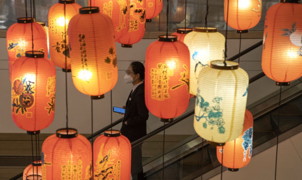 An office worker wearing a mask against coronavirus moves past lantern decorations in a mall and of...