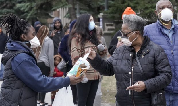 A worker hands out disinfectant wipes and pens as voters line up outside Riverside High School for ...