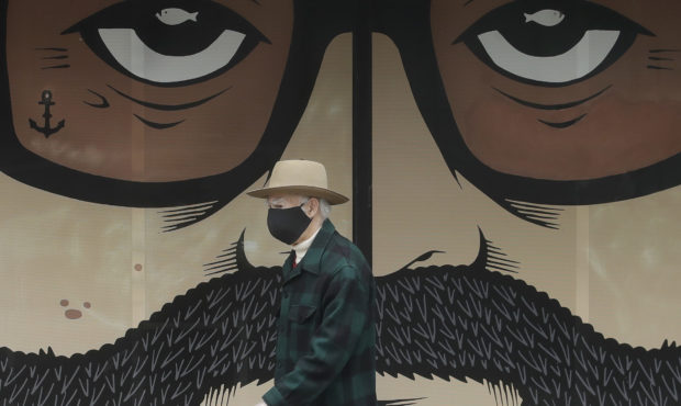 FILE - In this April 16, 2020, file photo, a man wears a mask while walking in front of a closed bu...