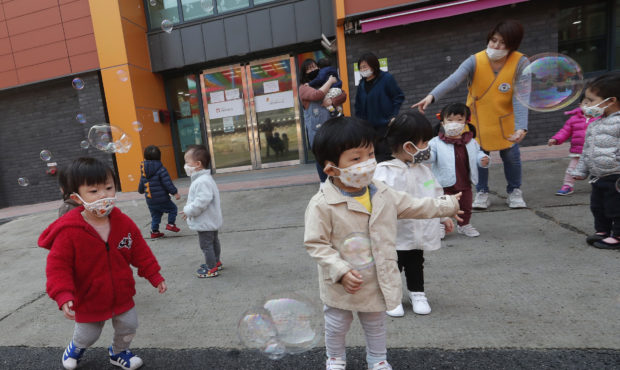 Children wearing face masks to help protect against the spread of the new coronavirus watch soap bu...