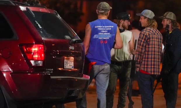 A group holds rifles as they watch protesters on the street Tuesday, Aug. 25, 2020, in Kenosha, Wis...