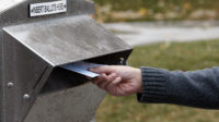 A person's hand is photographed dropping a ballot into a Utah drop box.