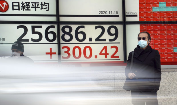 Men wearing masks against the spread of the coronavirus stand near an electronic stock board showin...