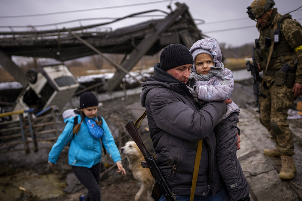 Local militiaman Valery, 37, carries a child as he helps a fleeing family across a bridge destroyed...