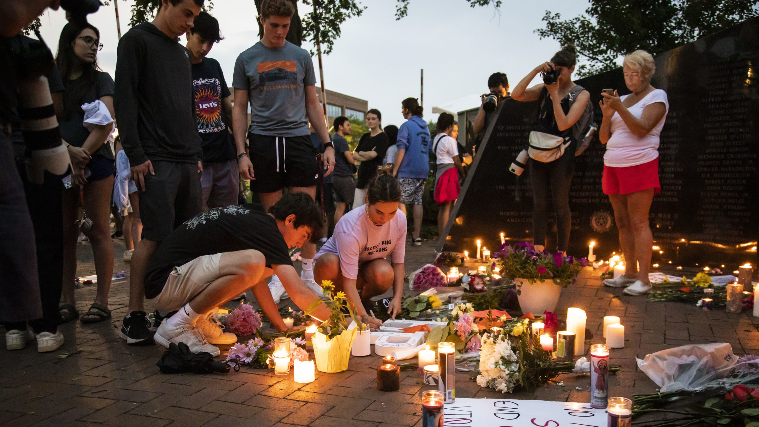 highland park mourners gather around a memorial...