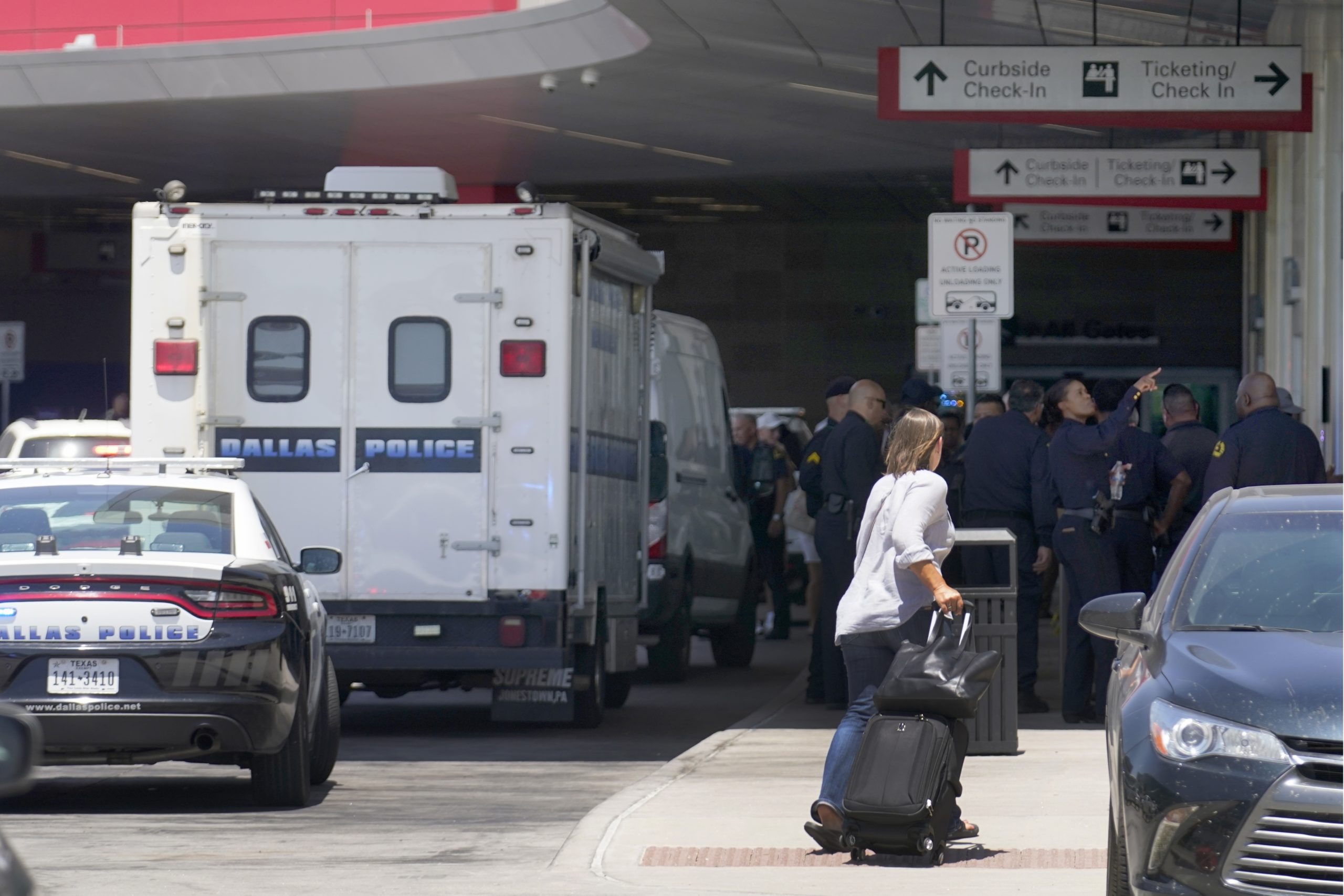 A traveler makes her way past emergency responders standing outside the ticketing and check in area...