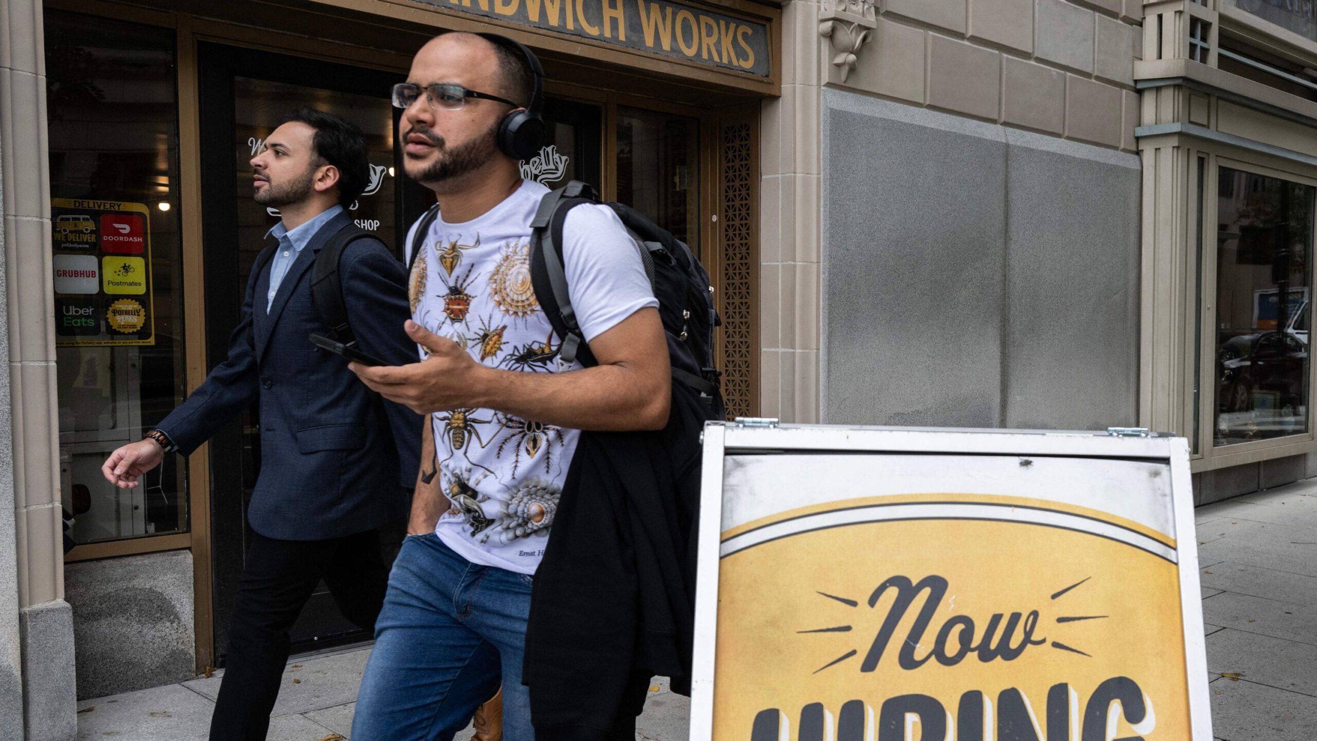 a man walks past a now hiring sign...