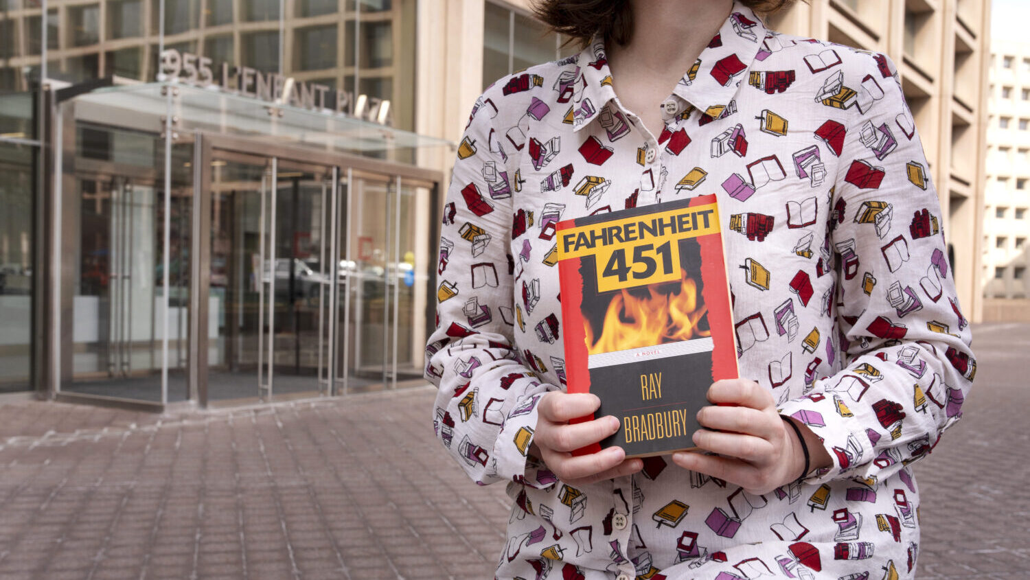 A person wearing a shirt covered in books holds a copy of the novel "Fahrenheit 451" while protesti...