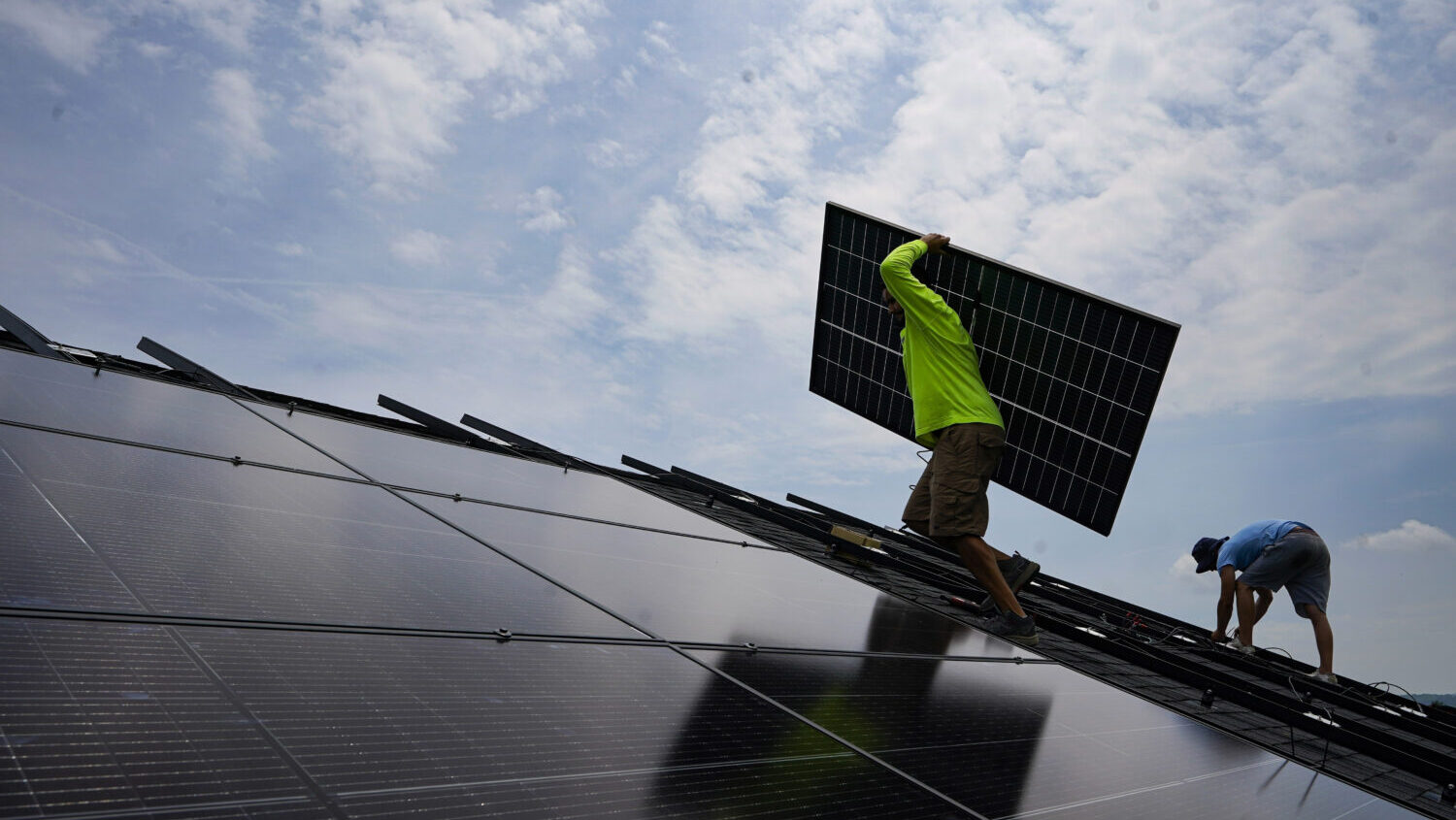 FILE - Nicholas Hartnett, owner of Pure Power Solar, carries a panel as he and Brian Hoeppner, righ...