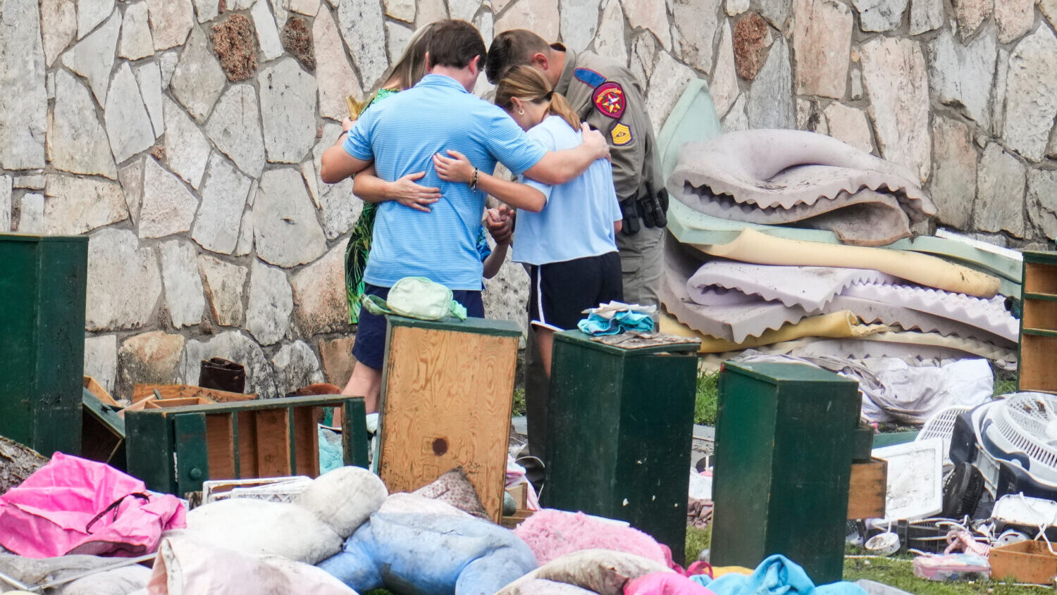 FILE - An officer prays with a family as they pick up items at Camp Mystic in Hunt, Texas, July 9, ...
