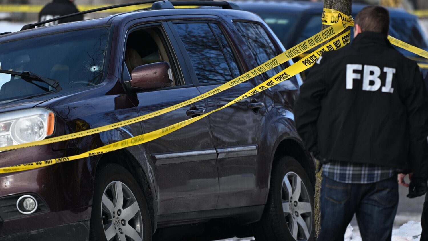 A bullet hole is seen in the windshield as law enforcement officers work the scene of a shooting in...