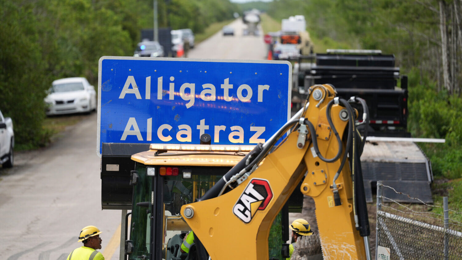 A loader holds a sign reading "Alligator Alcatraz" in its bucket as workers install it at the entra...