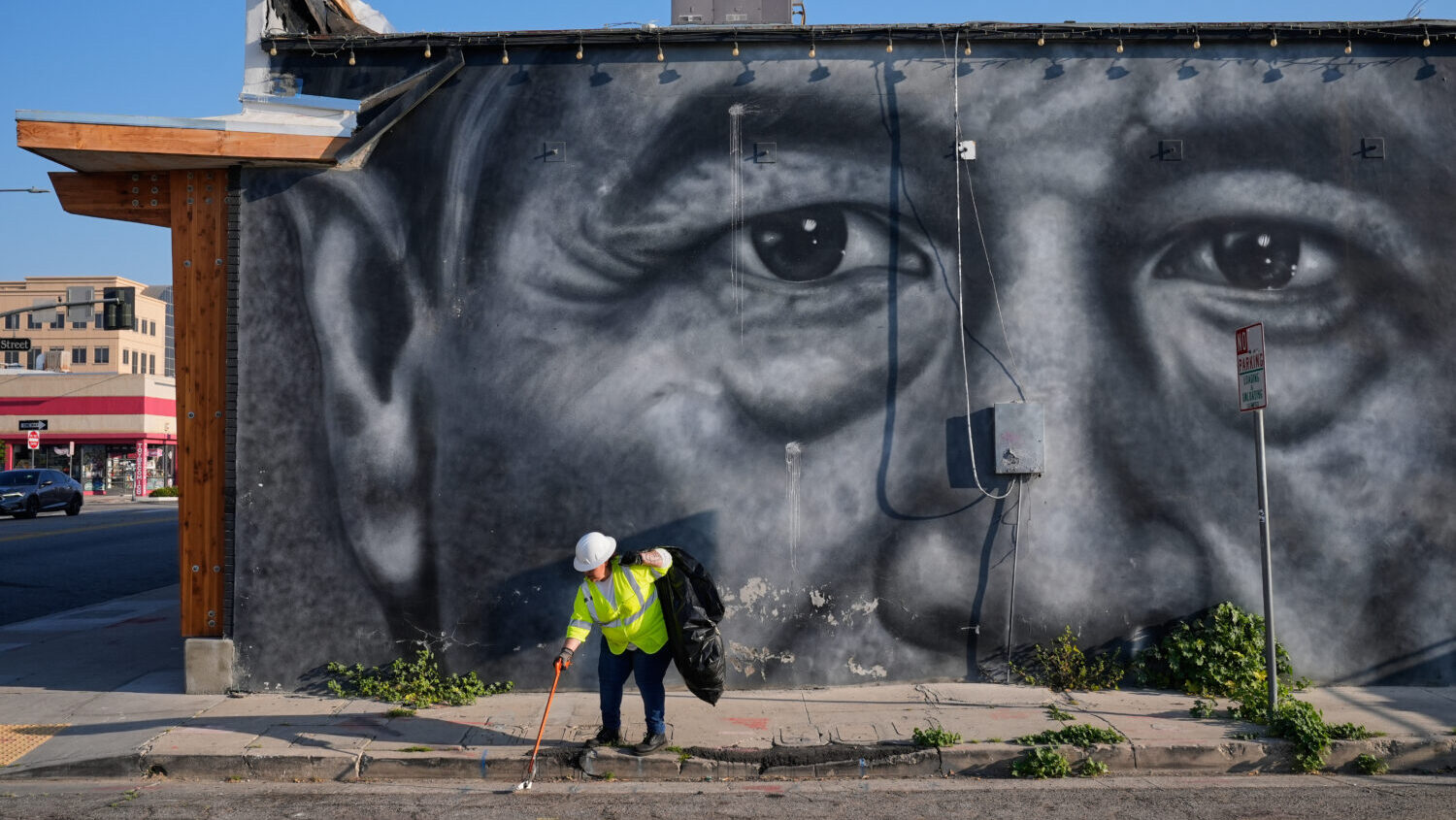 A sanitation worker picks up trash next to a mural of César Chavez in Bakersfield, Calif., Thursda...