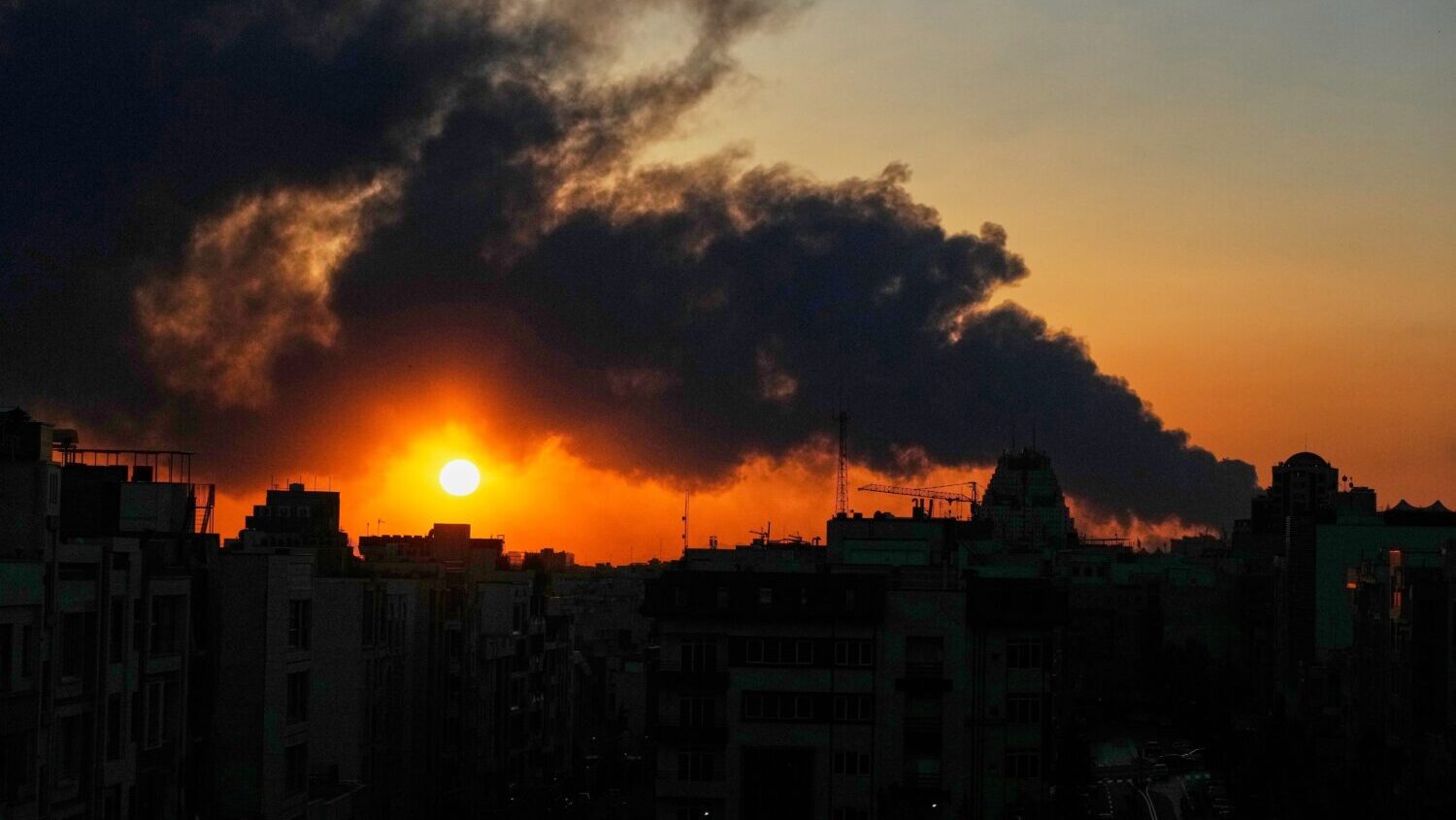 The sun sets behind a plume of smoke rising after a U.S.–Israeli military strike in Tehran, Iran,...