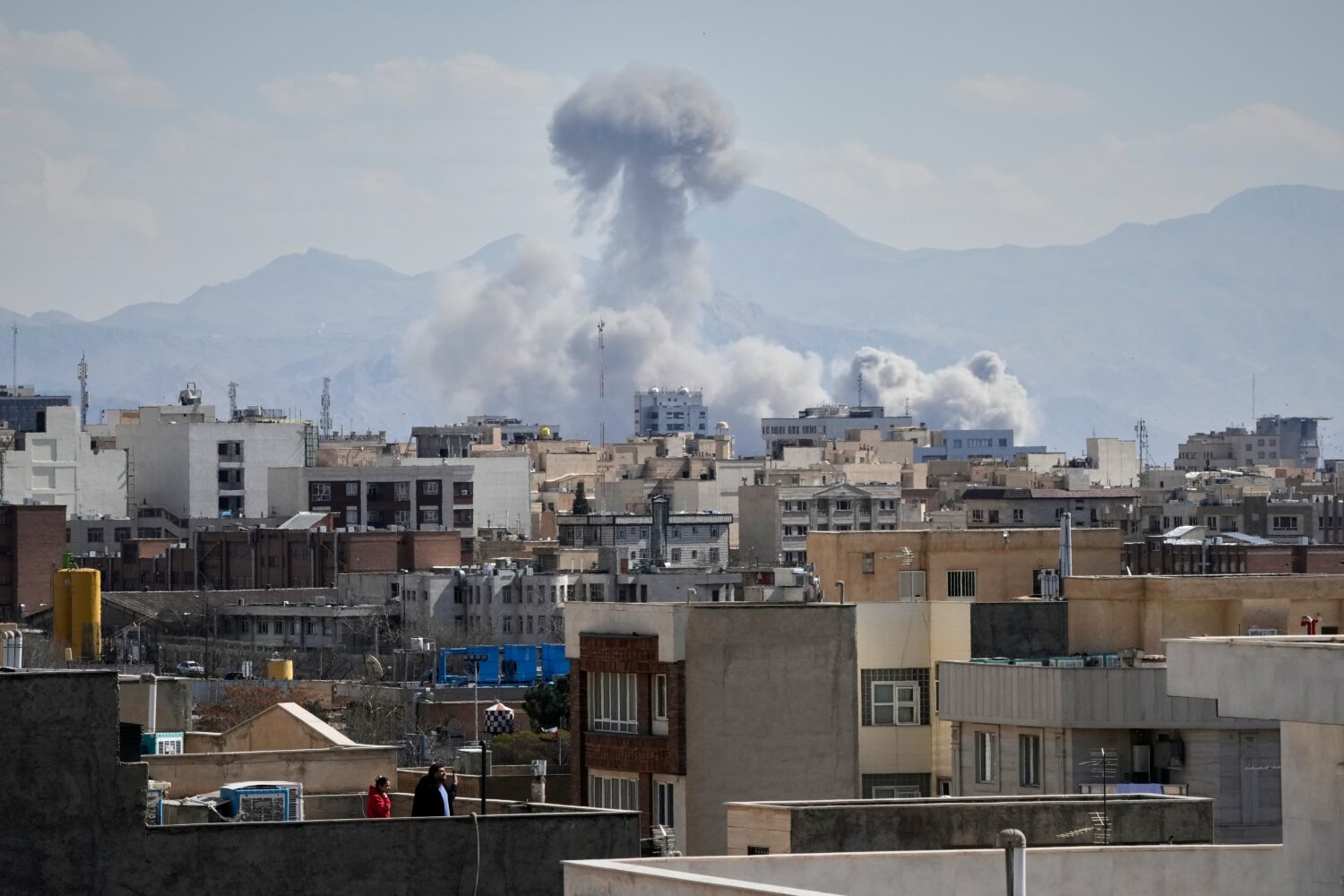 People watch from a rooftop as a plume of smoke rises after a strike in Tehran, Iran, Sunday, March...