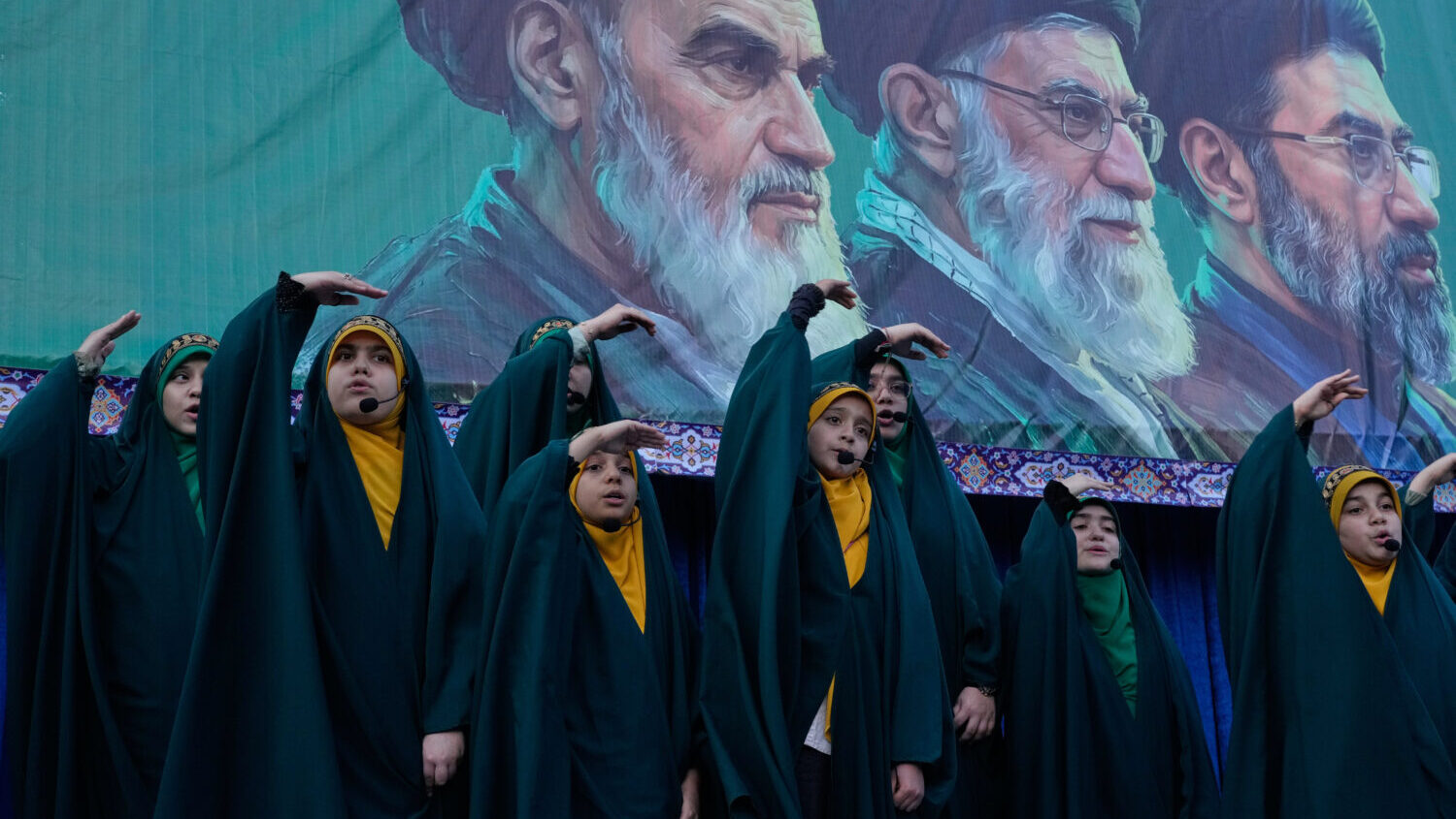 Girls sing a song as they show the movement of missiles with their hands next to the portraits of t...
