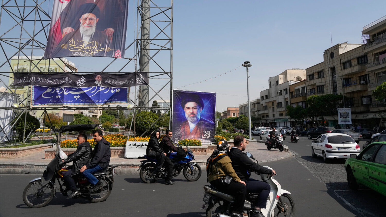 People drive their motorbikes past billboards showing the Iran's Supreme Leader Ayatollah Mojtaba K...