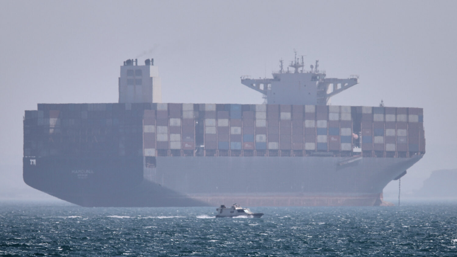 A container ship sits at anchor as a small motorboat passes in the foreground in the Strait of Horm...