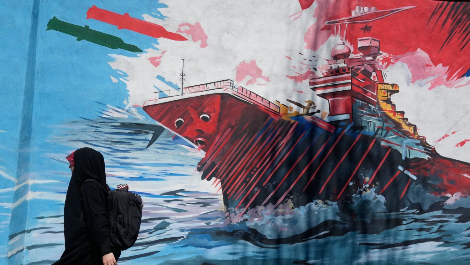 A woman walks past a mural depicting a U.S. aircraft carrier under missile attack in downtown Tehra...